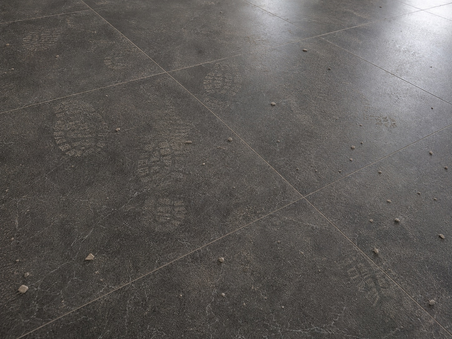 Dark grey tile floor marked by footprints, dust and construction debris before cleaning