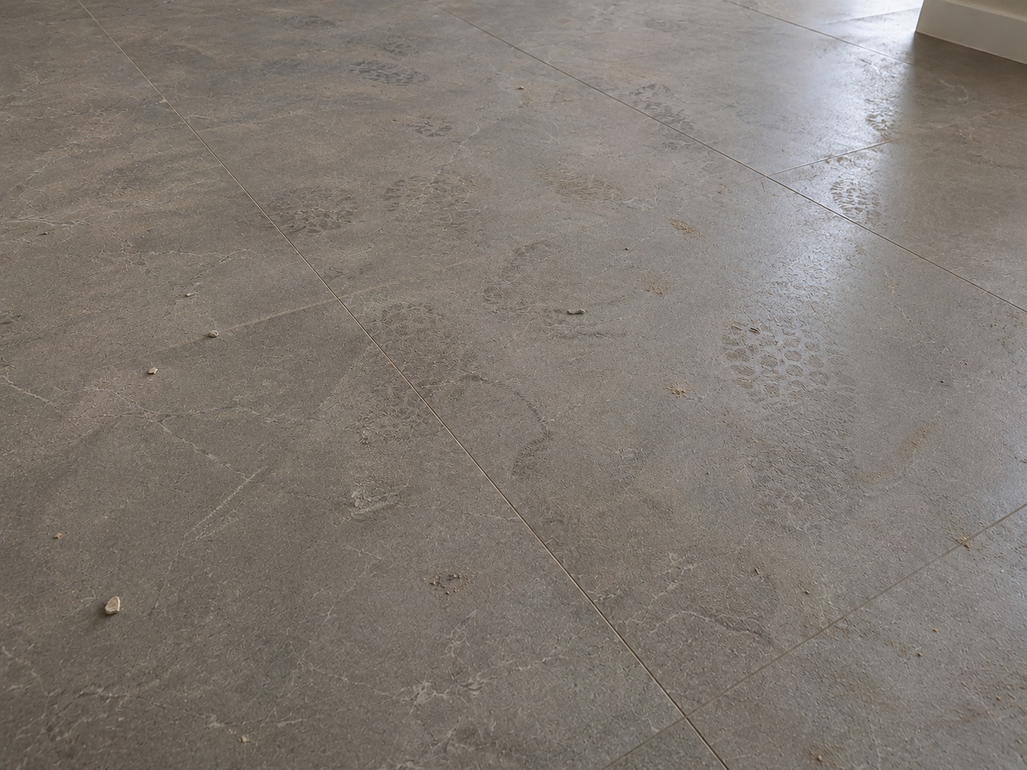 Light grey tile floor with construction footprints and dust before cleaning
