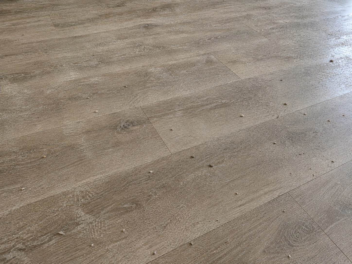 Vinyl plank floor covered with construction dust and loose debris before cleaning