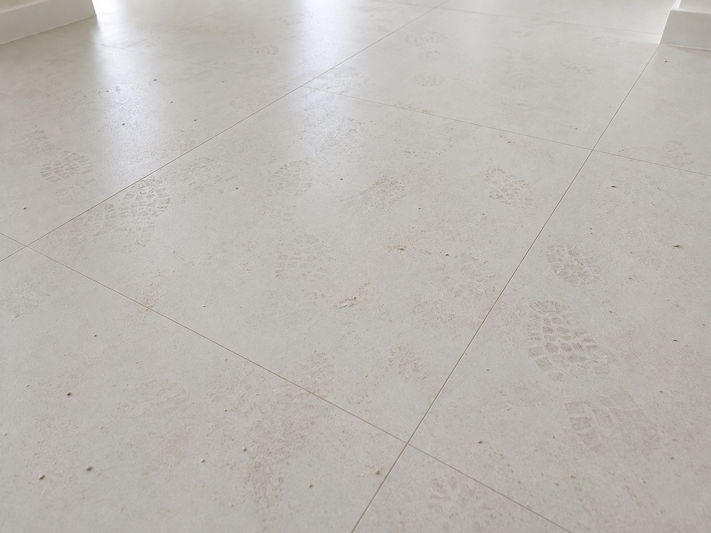 White tile floor with dusty footprints and construction residue before cleaning
