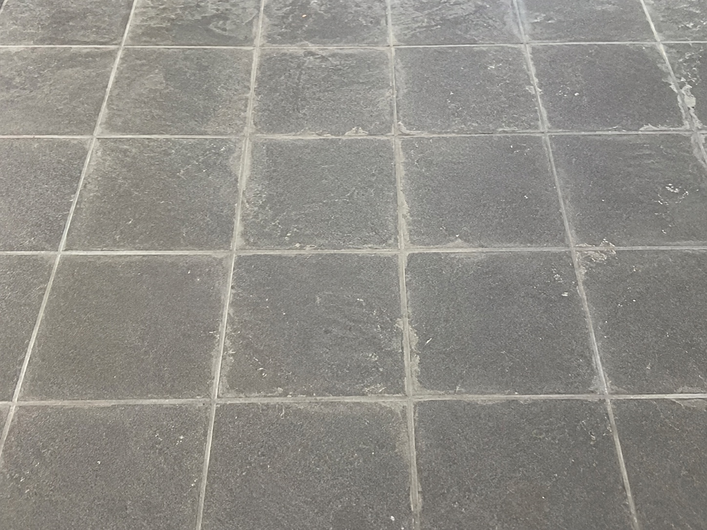 Dark tile floor with construction grout haze before cleaning
